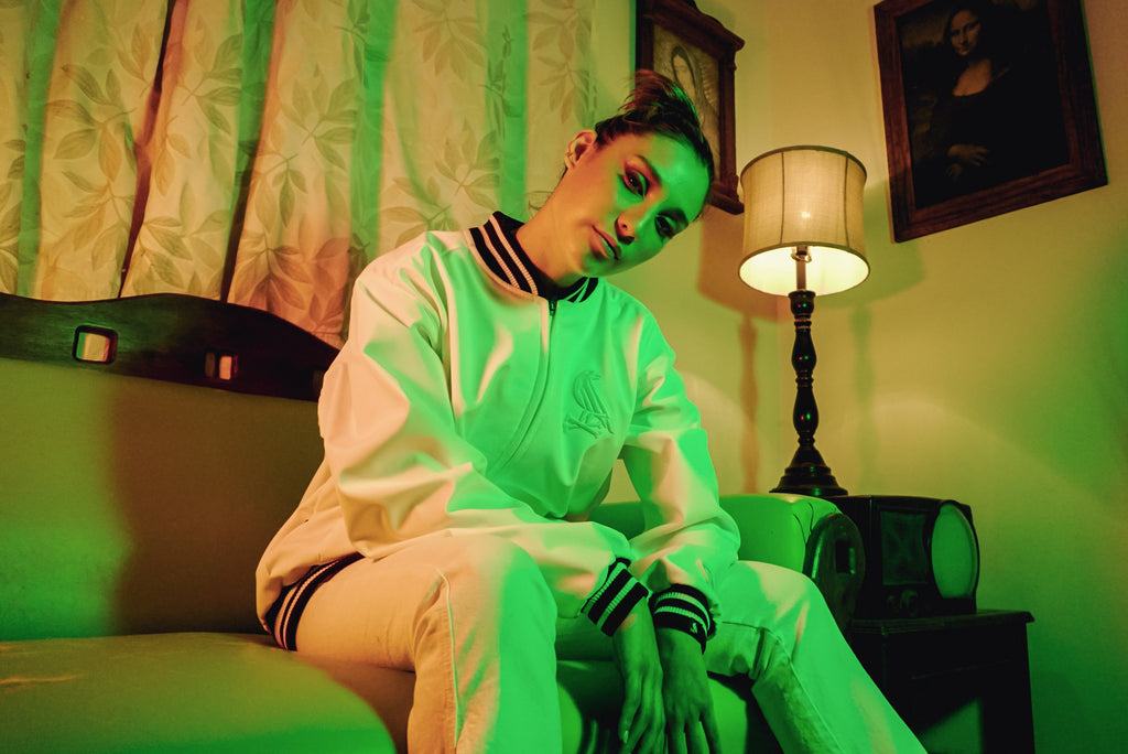 Female model wearing WHITE JACKET sitting on couch in neo phosphorescent lighting. First image of collection.