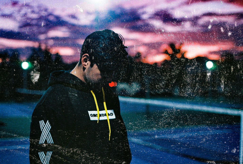 Man wearing Rainforrest hoodie by Crowdead, standing outside as the sun sets.