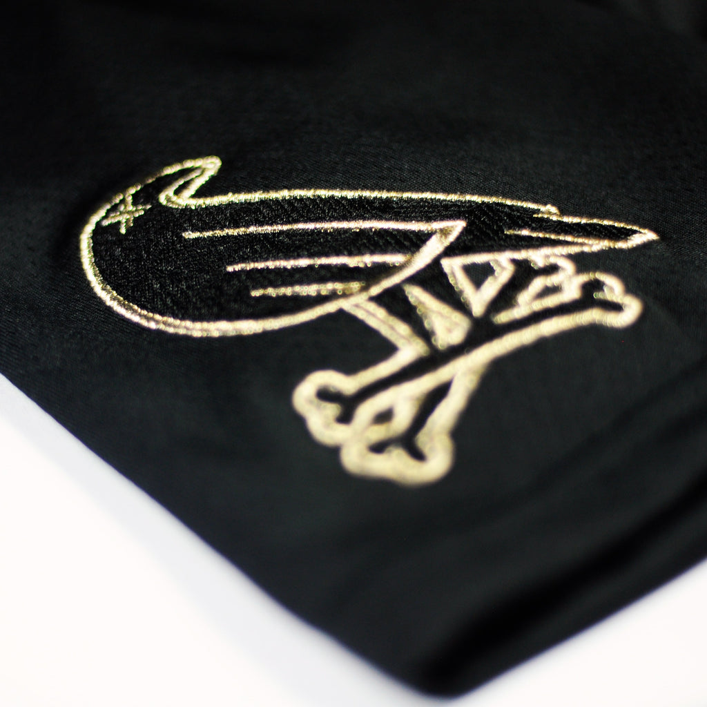 The new gold jersey by Crowdead. Sleeve Crow & Crossbones embroidered logo closeup.